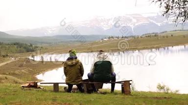 两个成年人的后景，坐在长凳上，花时间环顾山湖美景
